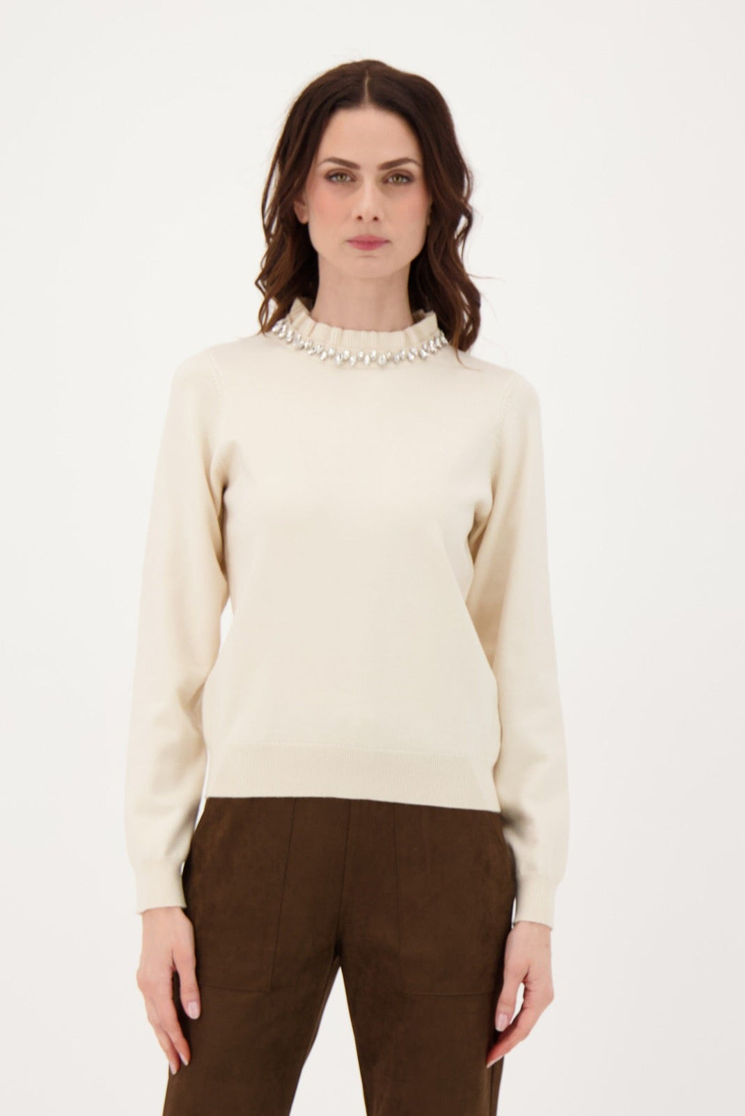 Woman wearing a cream sweater and brown pants on a white background