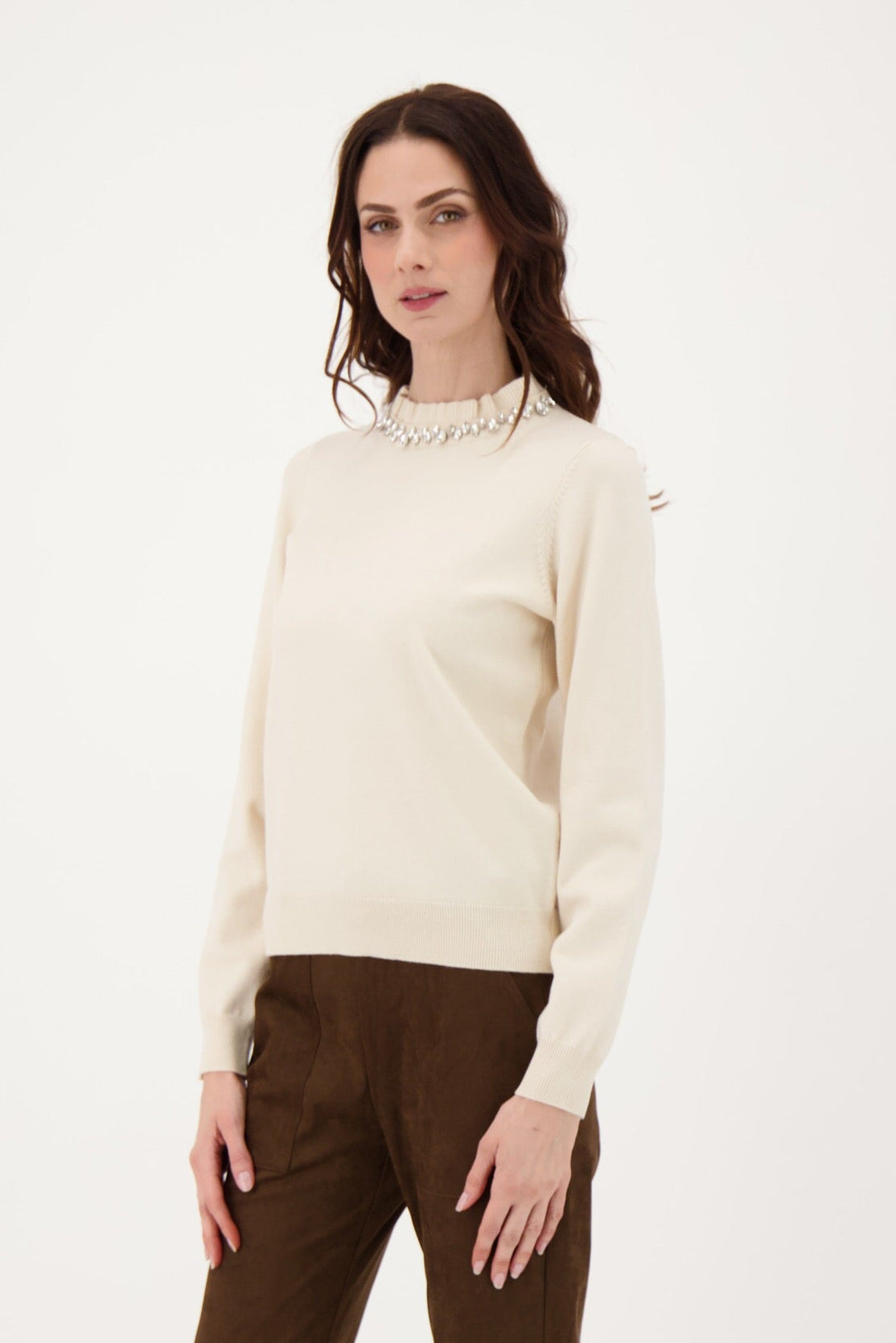 Woman wearing a cream sweater and brown pants on a white background