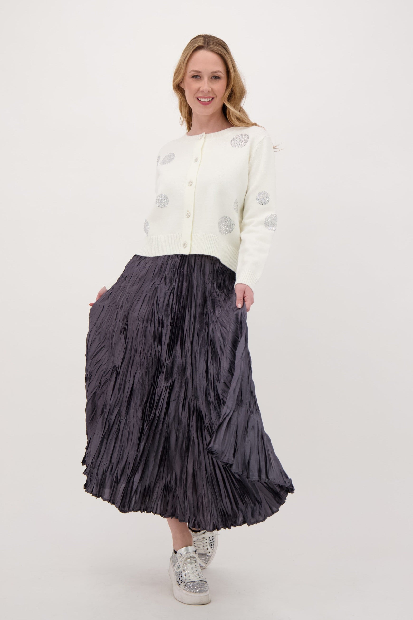 Woman wearing a white cardigan and black pleated skirt on a white background