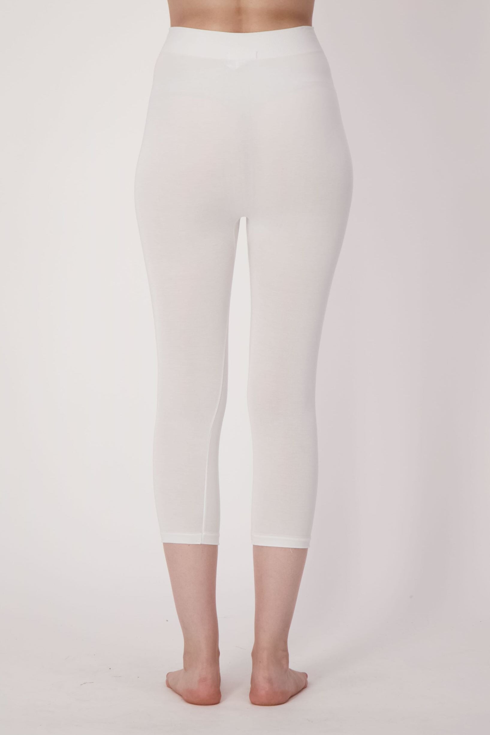Person wearing white leggings and a white top on a light pink background