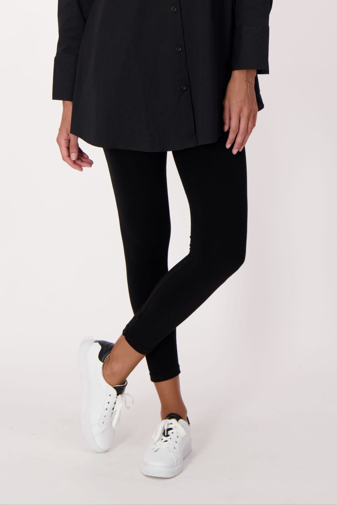 Person wearing a black coat, black pants, and white sneakers on a white background