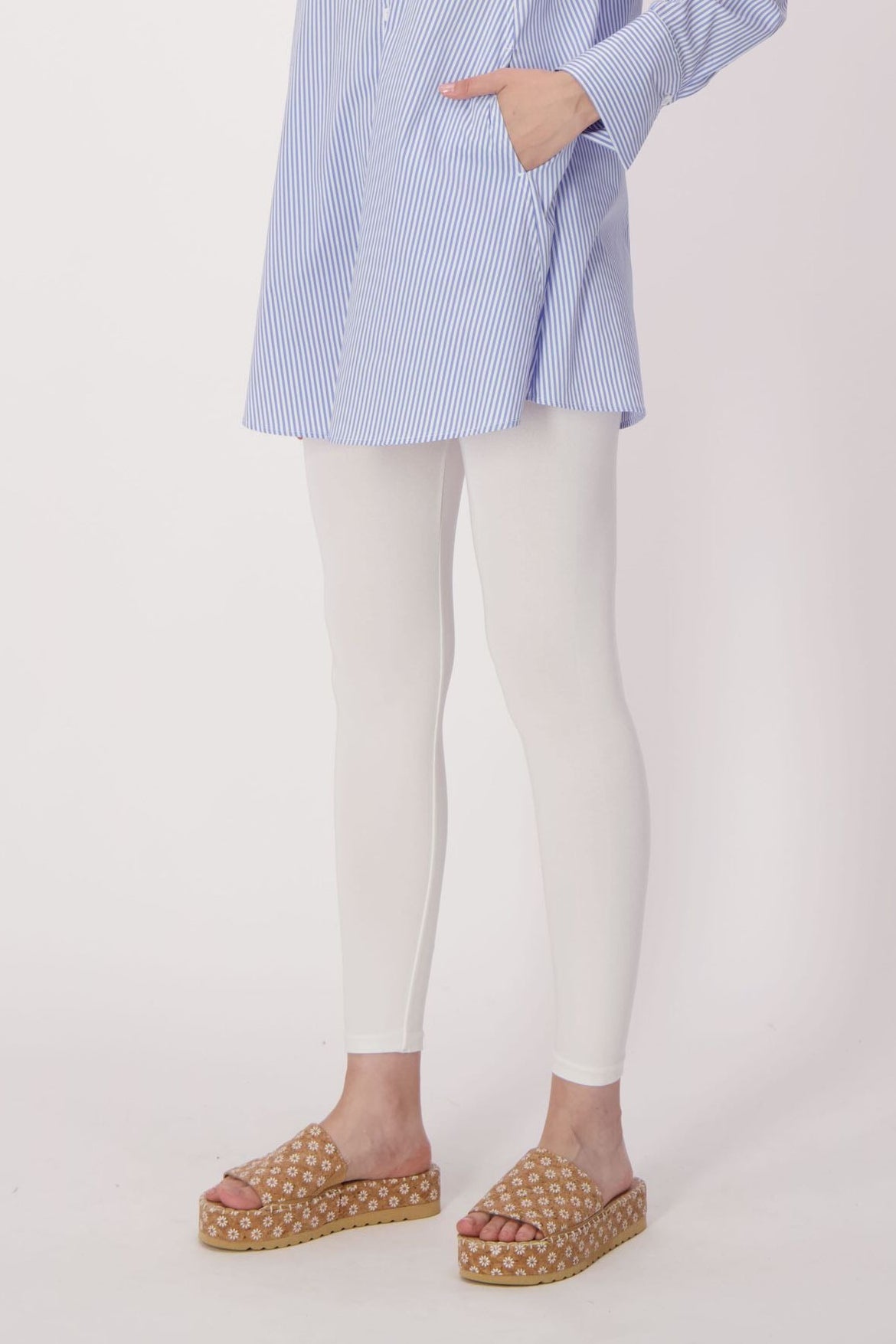 Person wearing a blue checkered shirt, white leggings, and patterned sandals on a light background