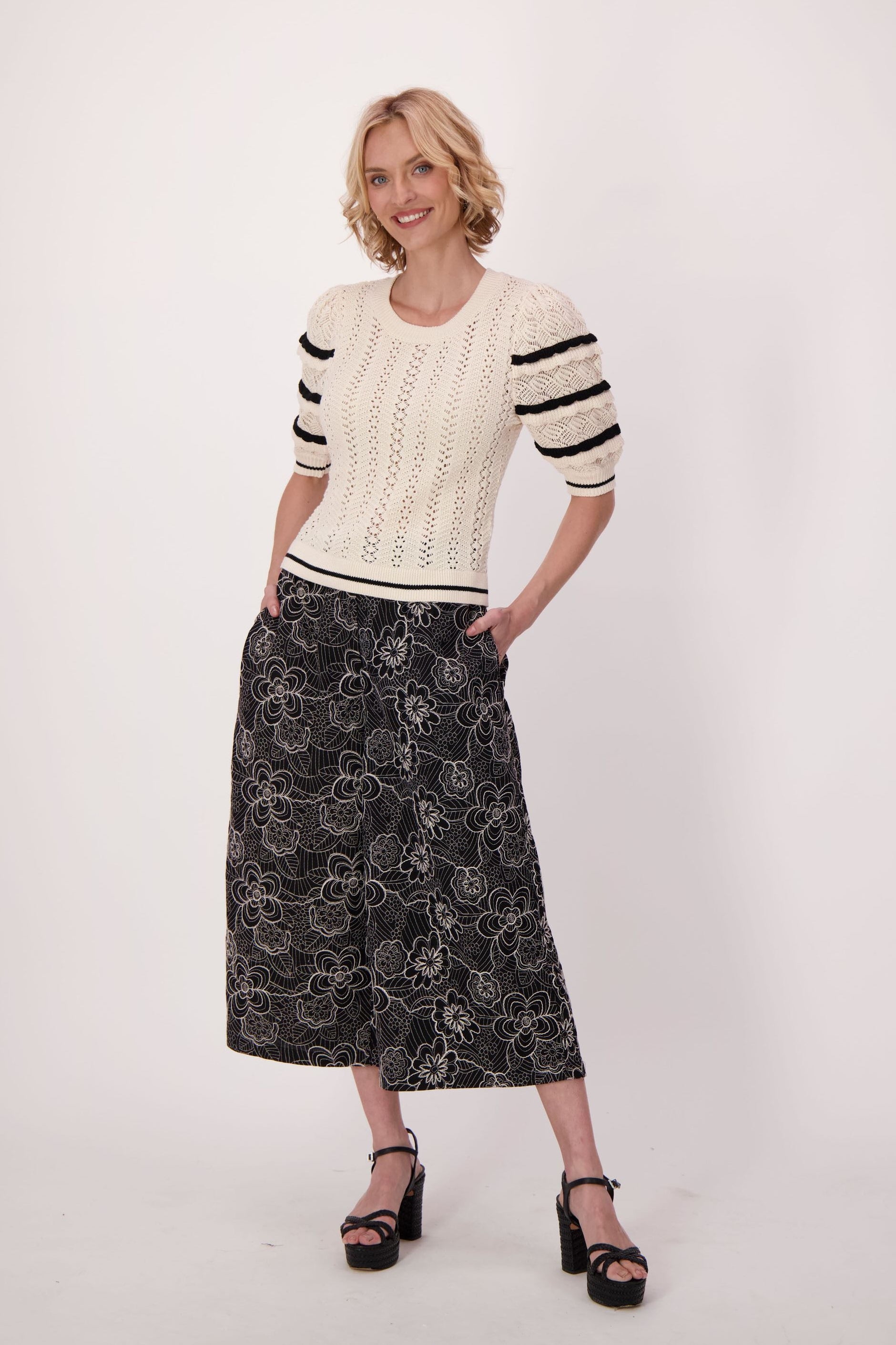 Woman wearing a cream sweater with black and white stripes and a black floral skirt on a white background
