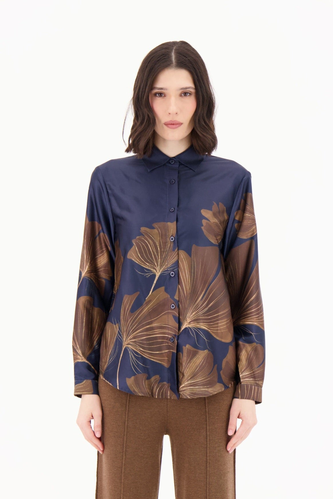 Woman wearing a blue and brown patterned top with brown flared pants on a white background