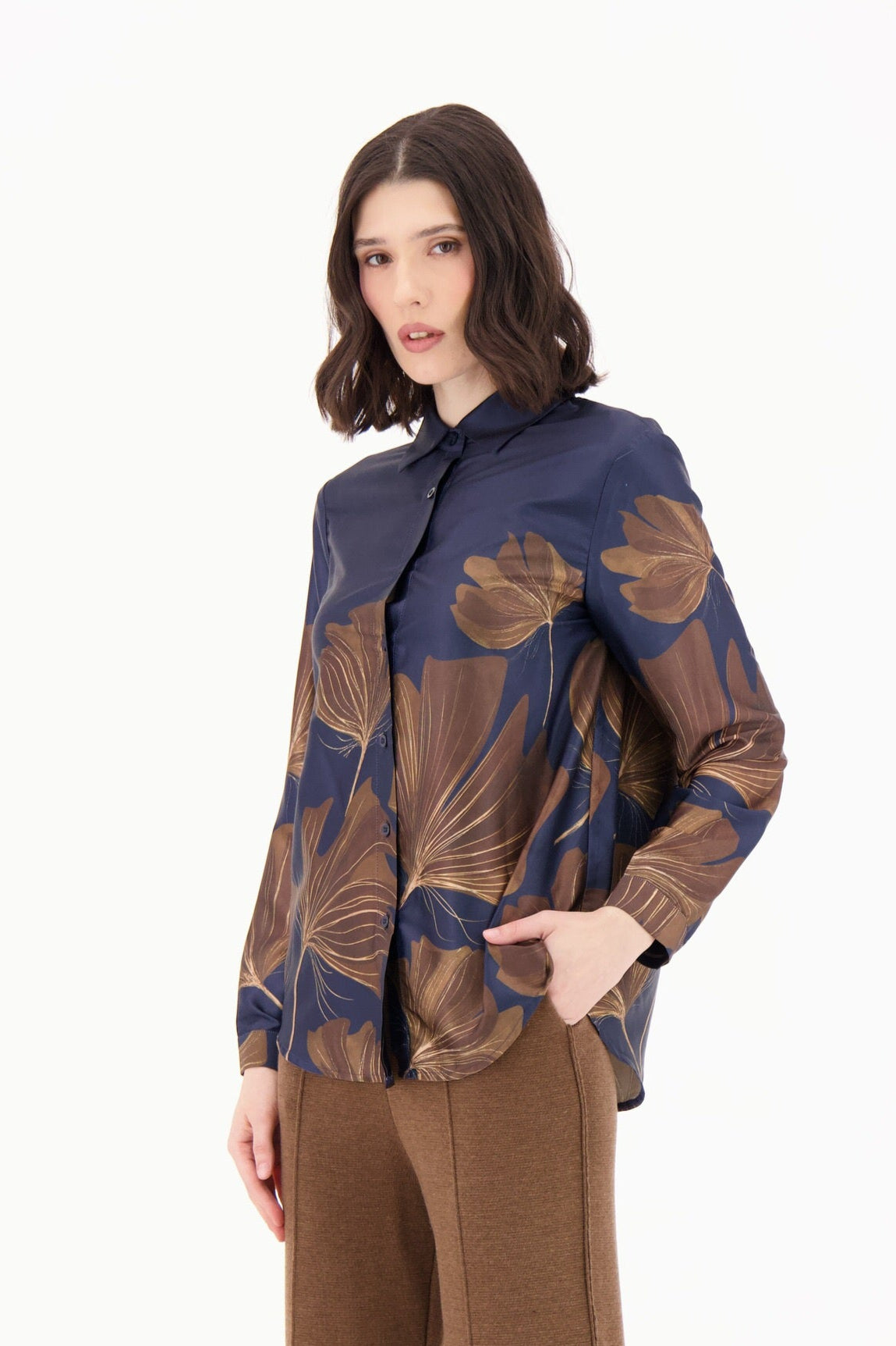 Woman wearing a patterned jacket and brown pants on a white background