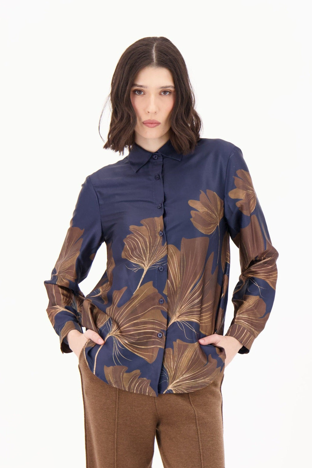 Woman wearing a patterned blouse and brown pants on a white background