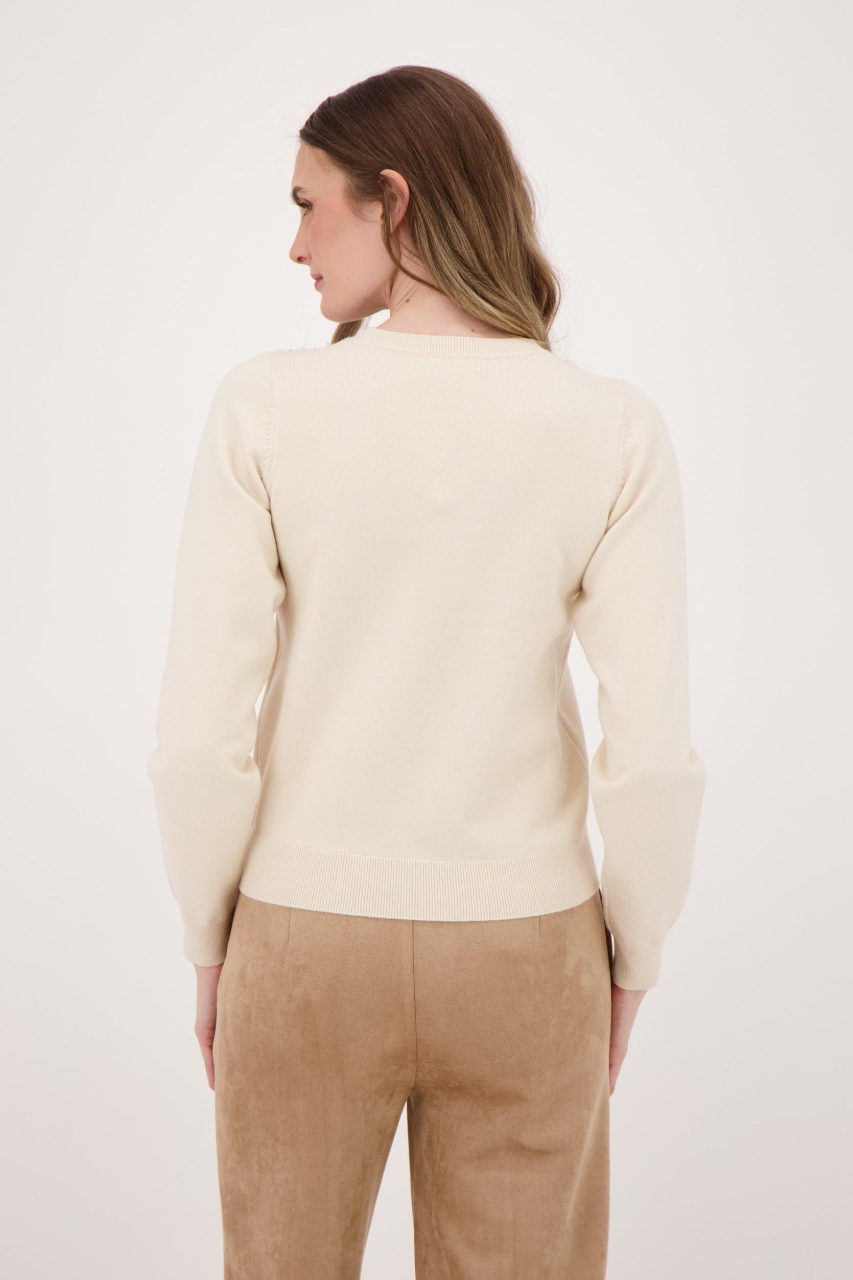Woman wearing a cream sweater and beige pants against a white background