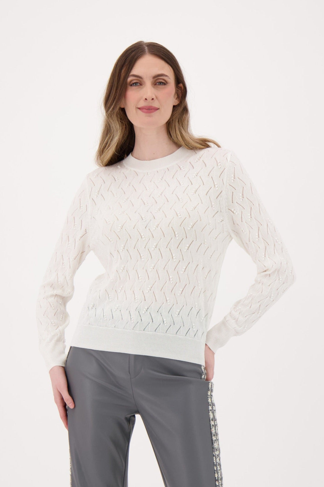 Woman wearing a white cable knit sweater and gray pants on a white background