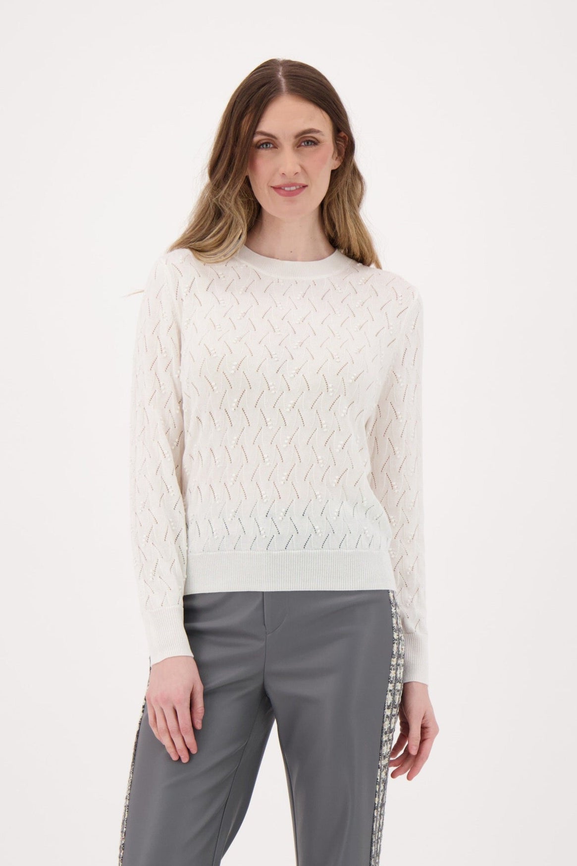 Woman wearing a white textured sweater and gray pants on a white background