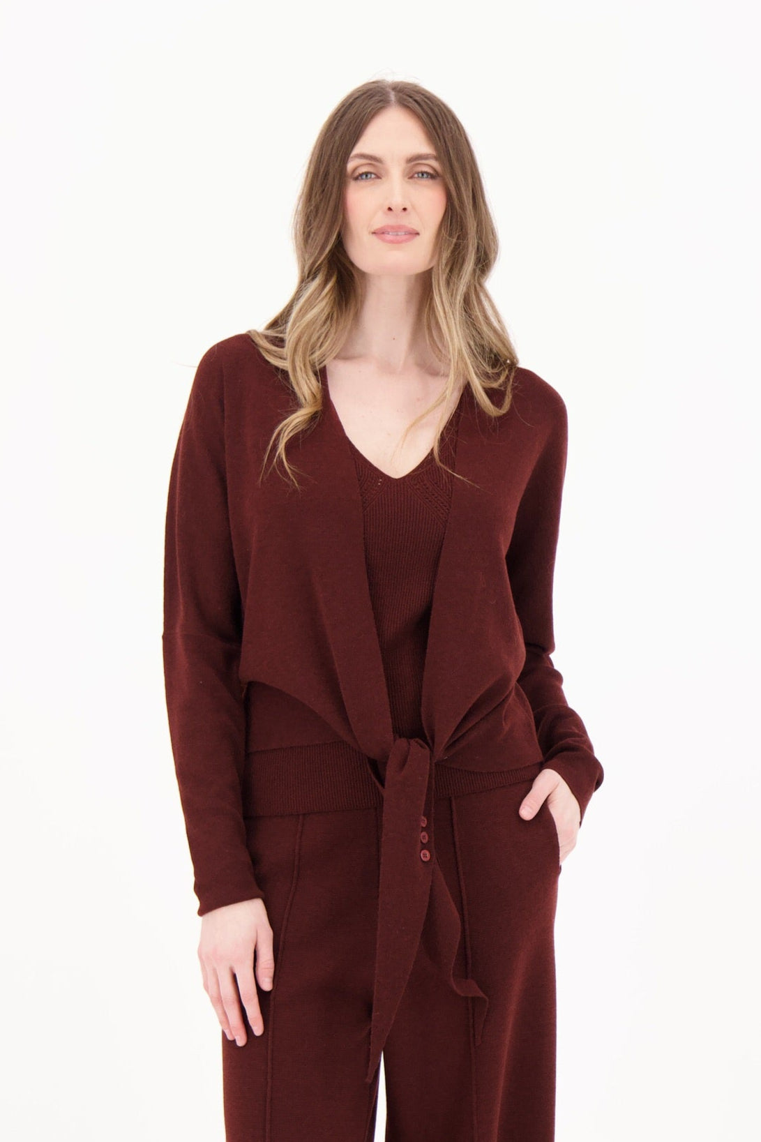 Woman wearing a maroon jumpsuit with a matching cardigan on a white background