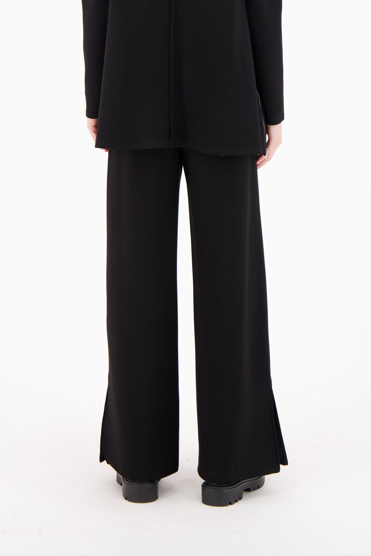 Person wearing a black suit standing against a white background