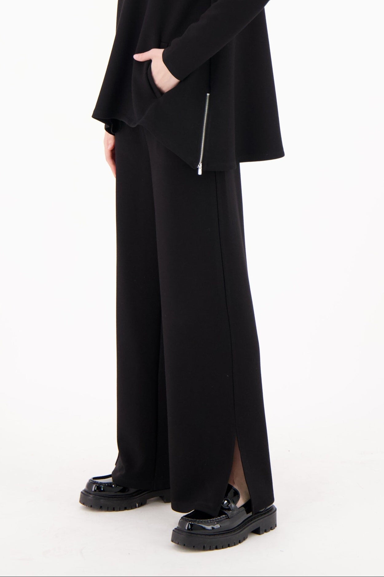 Person wearing a black outfit with a long coat and pants on a white background
