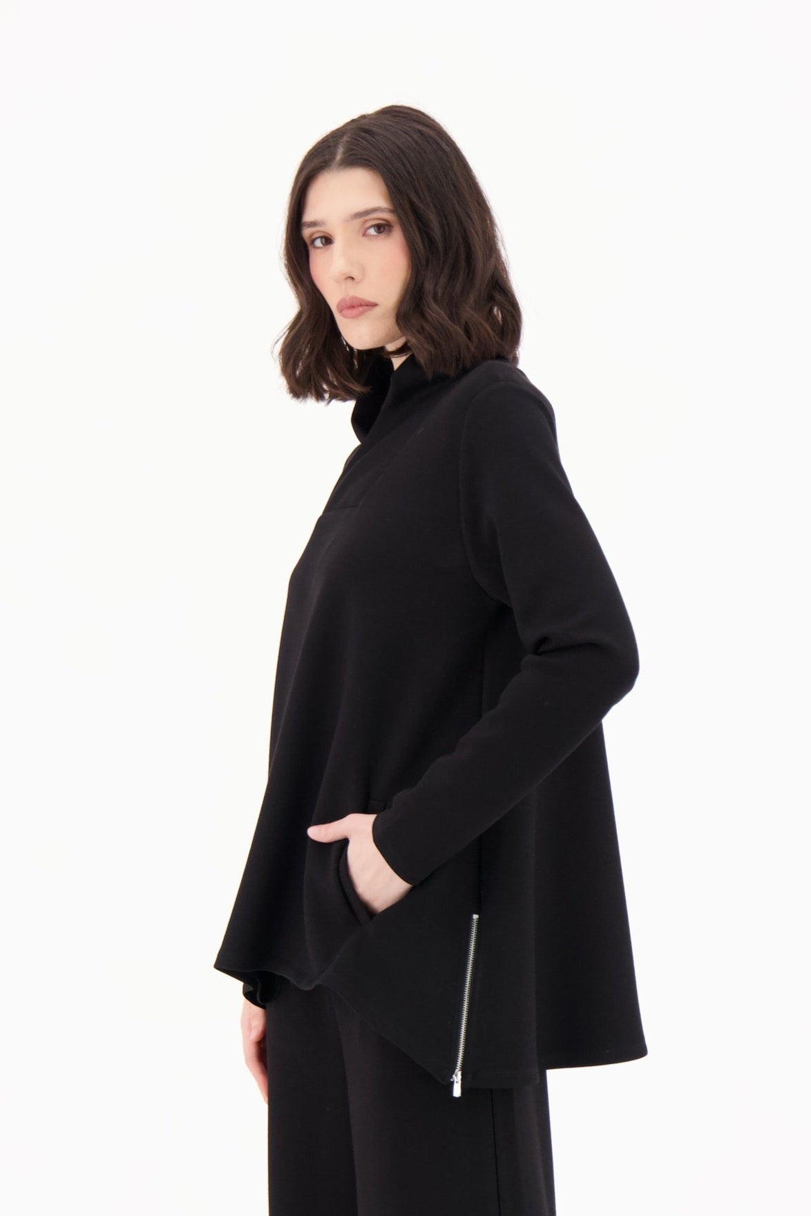 Person wearing a black outfit with a long coat and pants on a white background