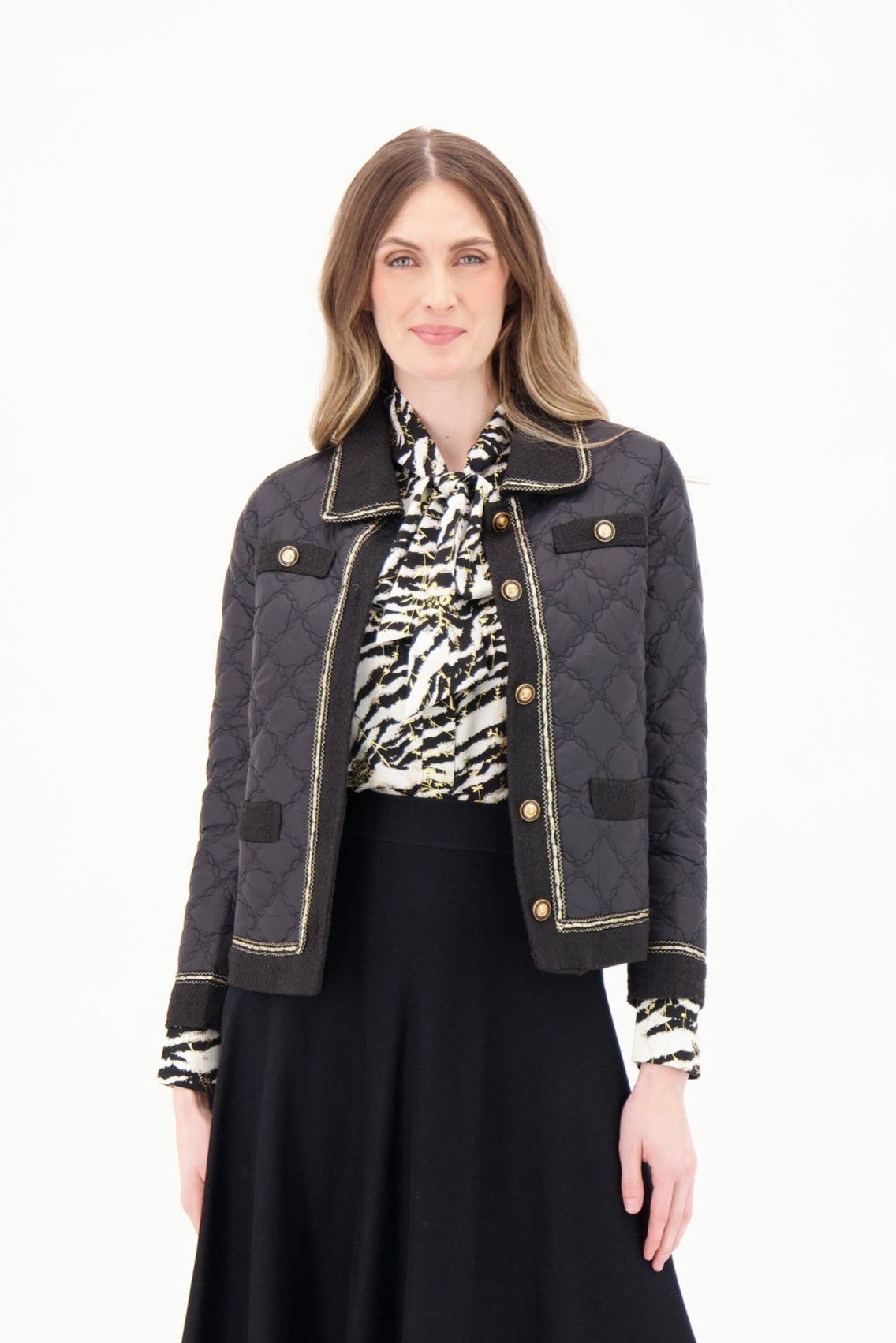 Woman wearing a black jacket, patterned shirt, and black skirt on a white background