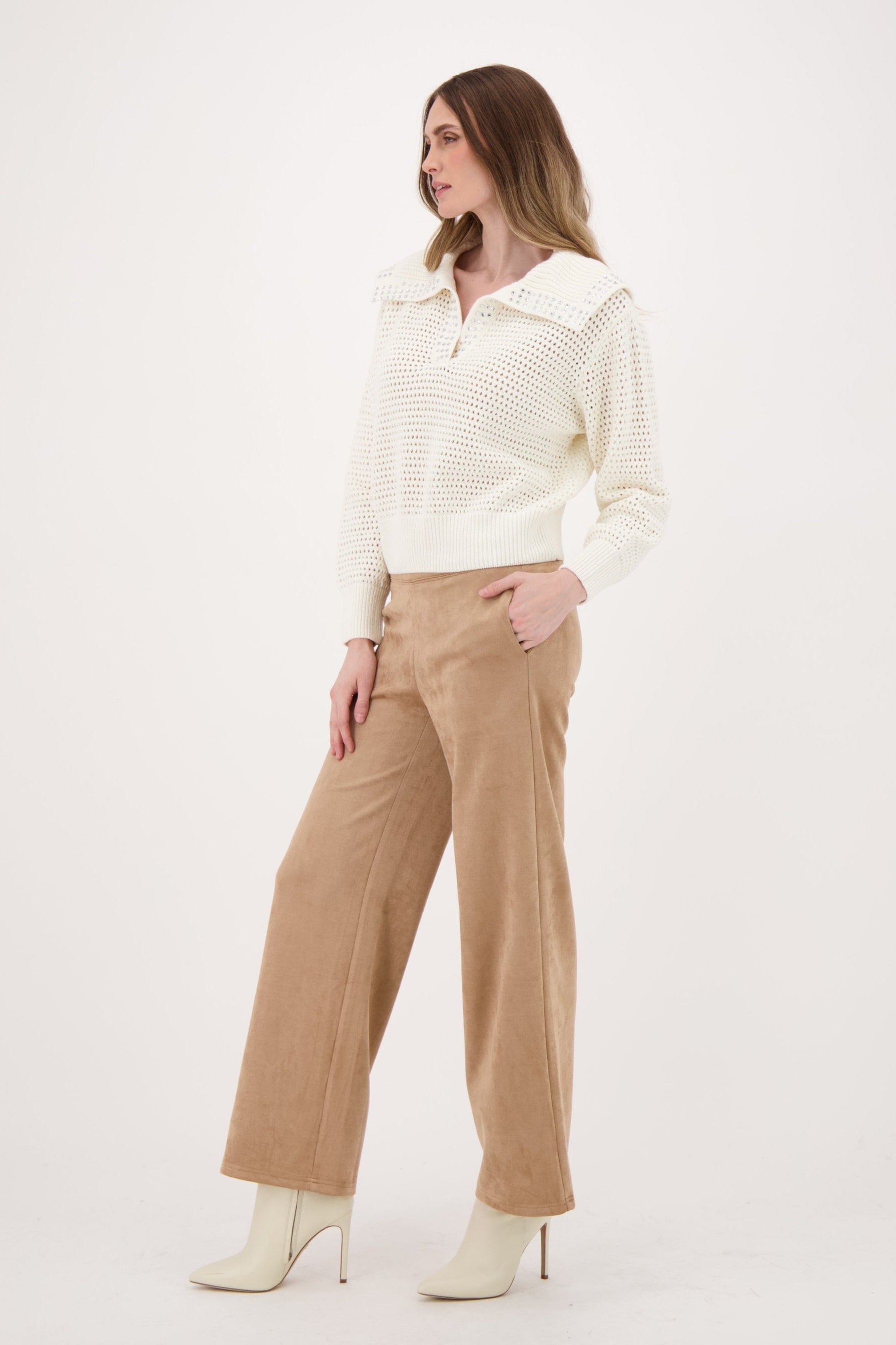 Woman wearing a cream ribbed sweater and beige pants on a white background