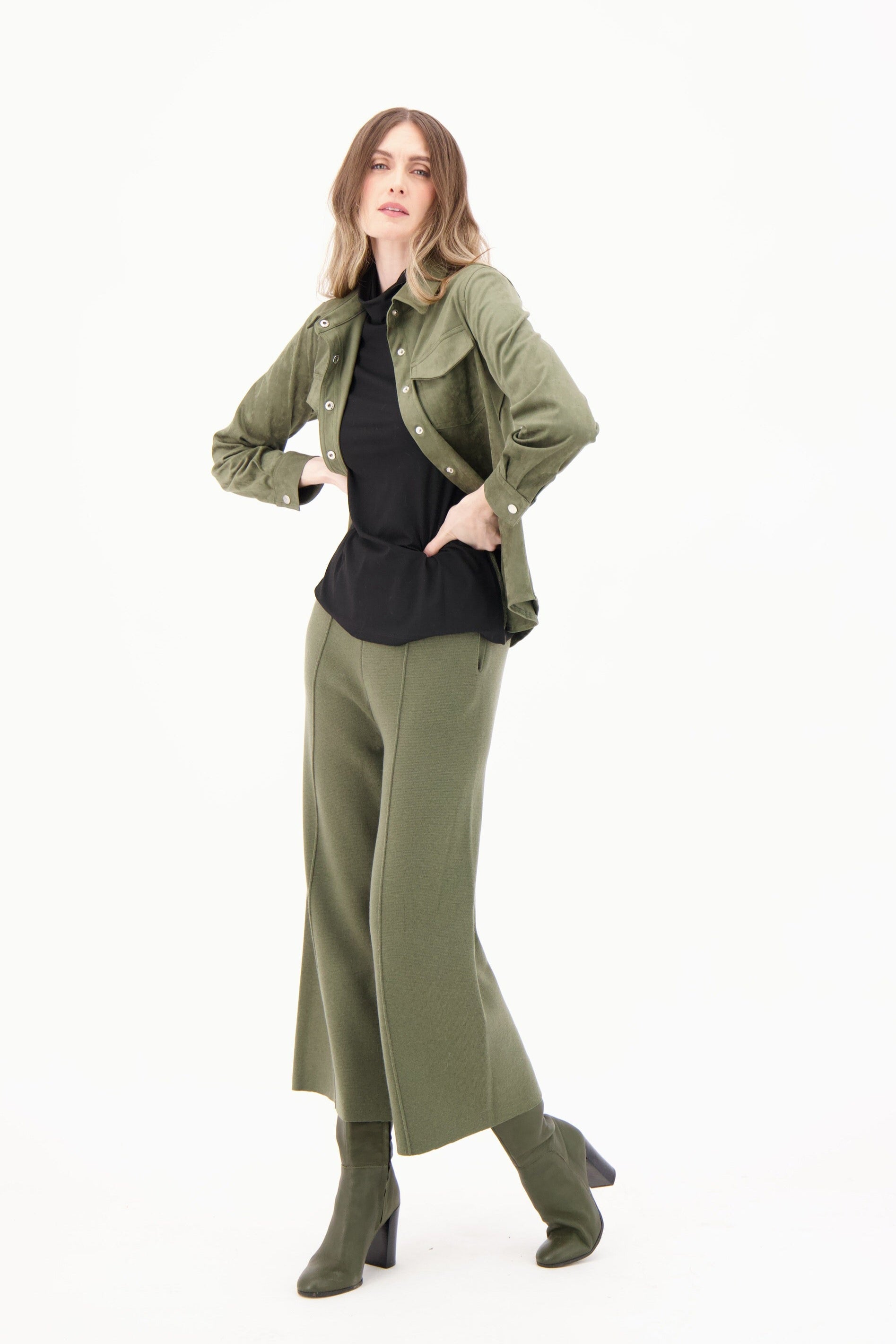 Woman wearing a green jacket, black top, and green pants on a white background