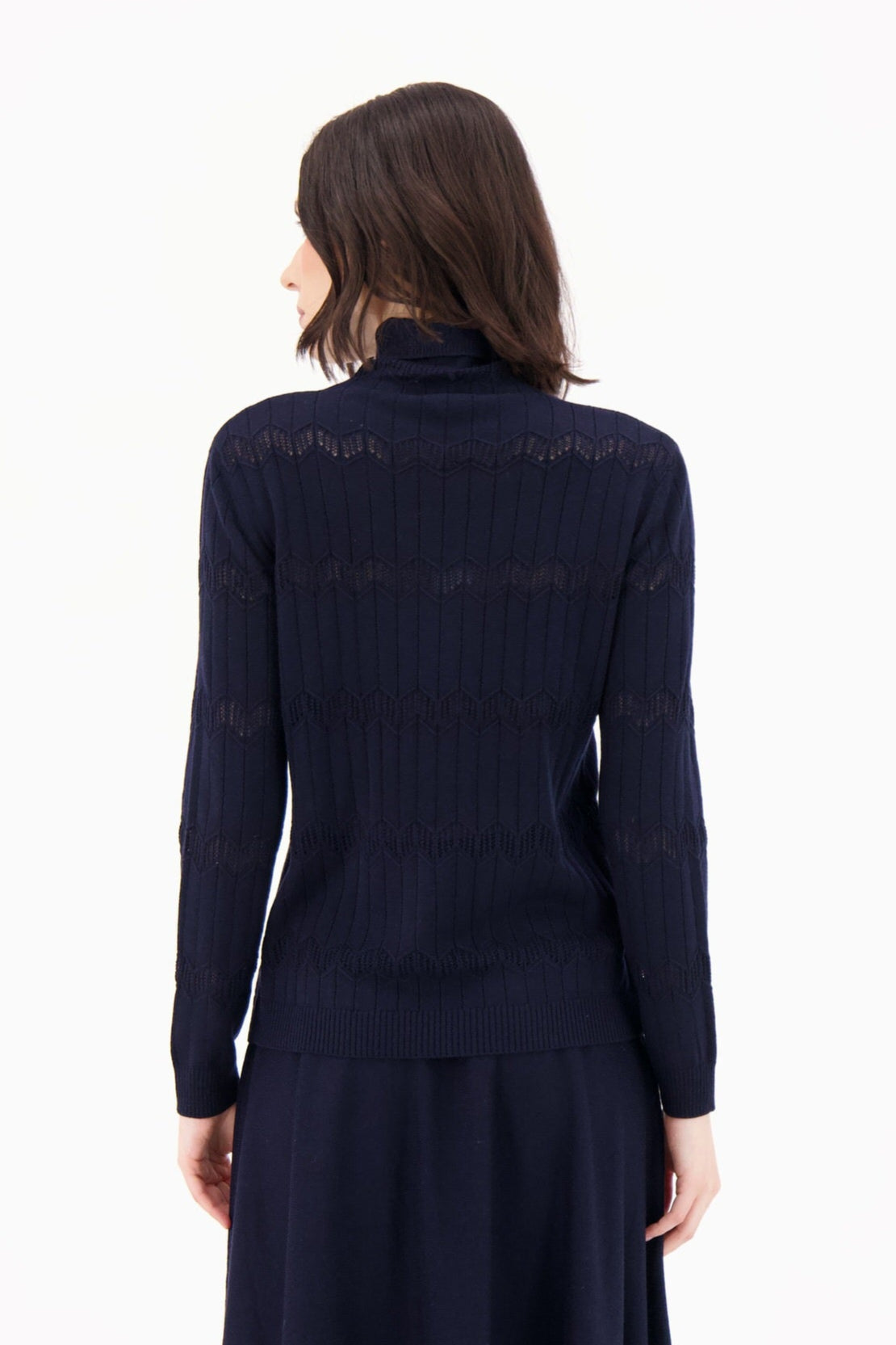 Woman wearing a dark blue ribbed dress with a turtleneck on a white background
