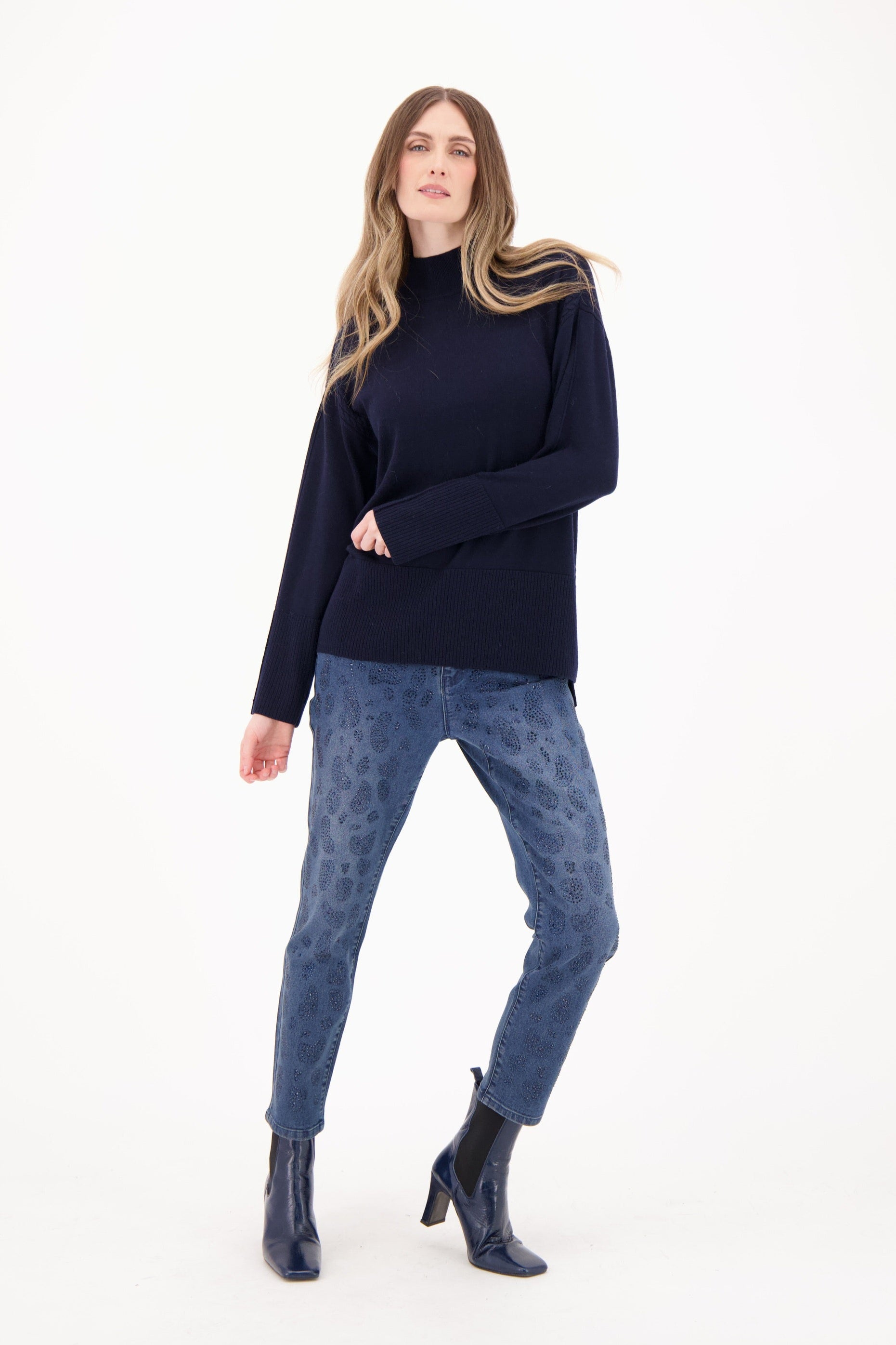 Woman wearing a navy sweater and patterned pants on a white background