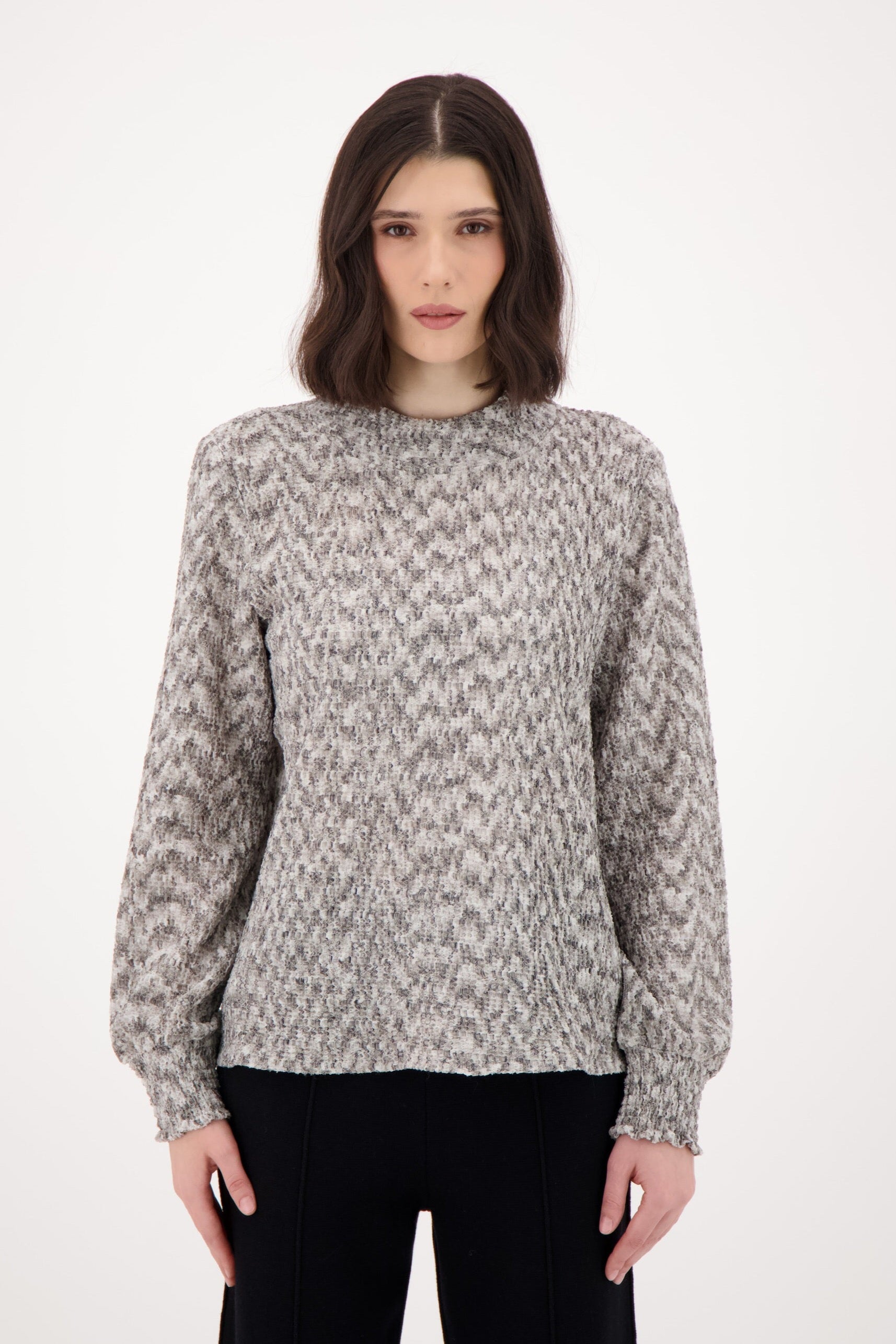 Woman wearing a patterned sweater and black pants on a white background