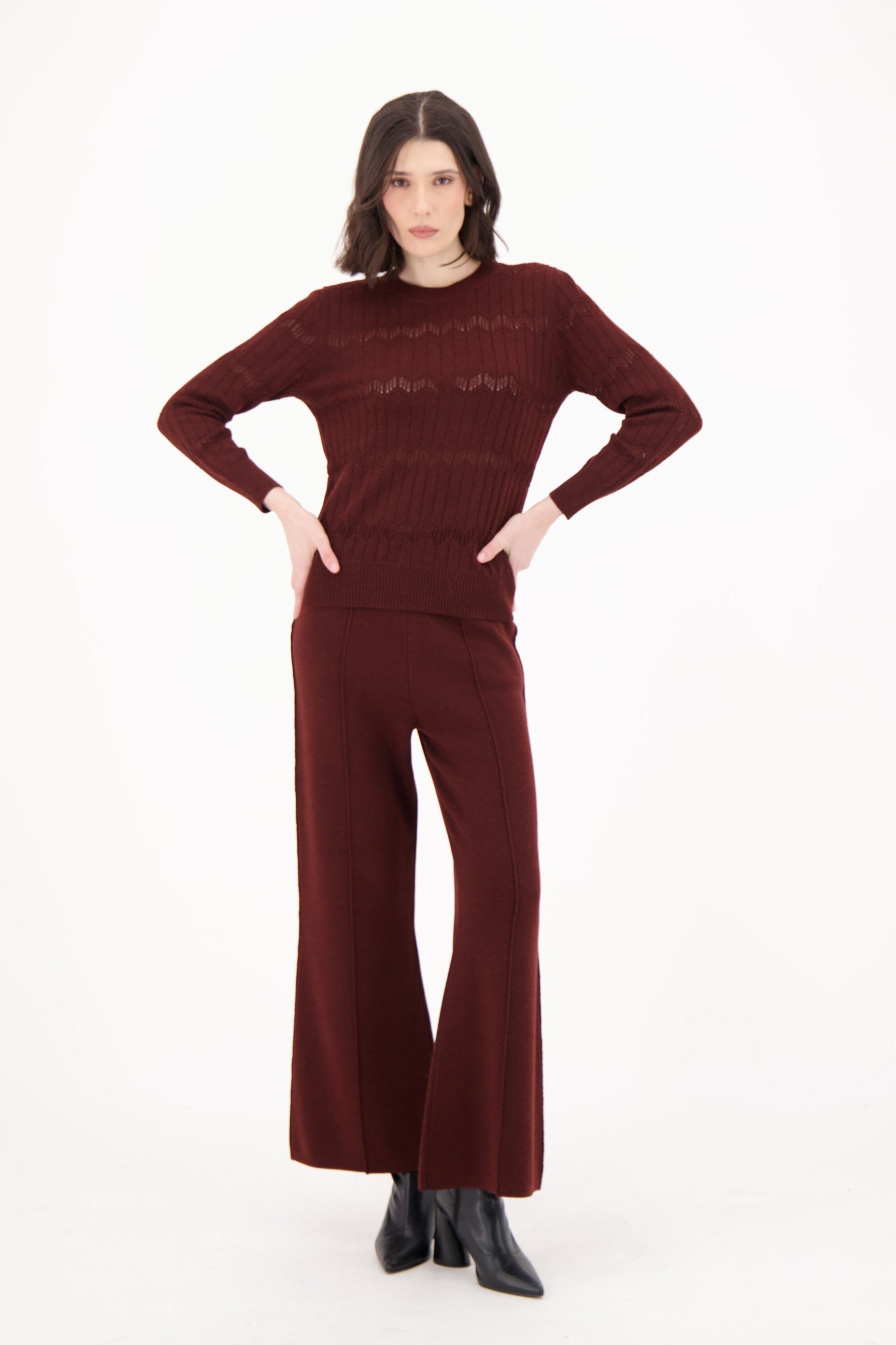 Woman wearing a maroon sweater and wide-leg pants on a white background