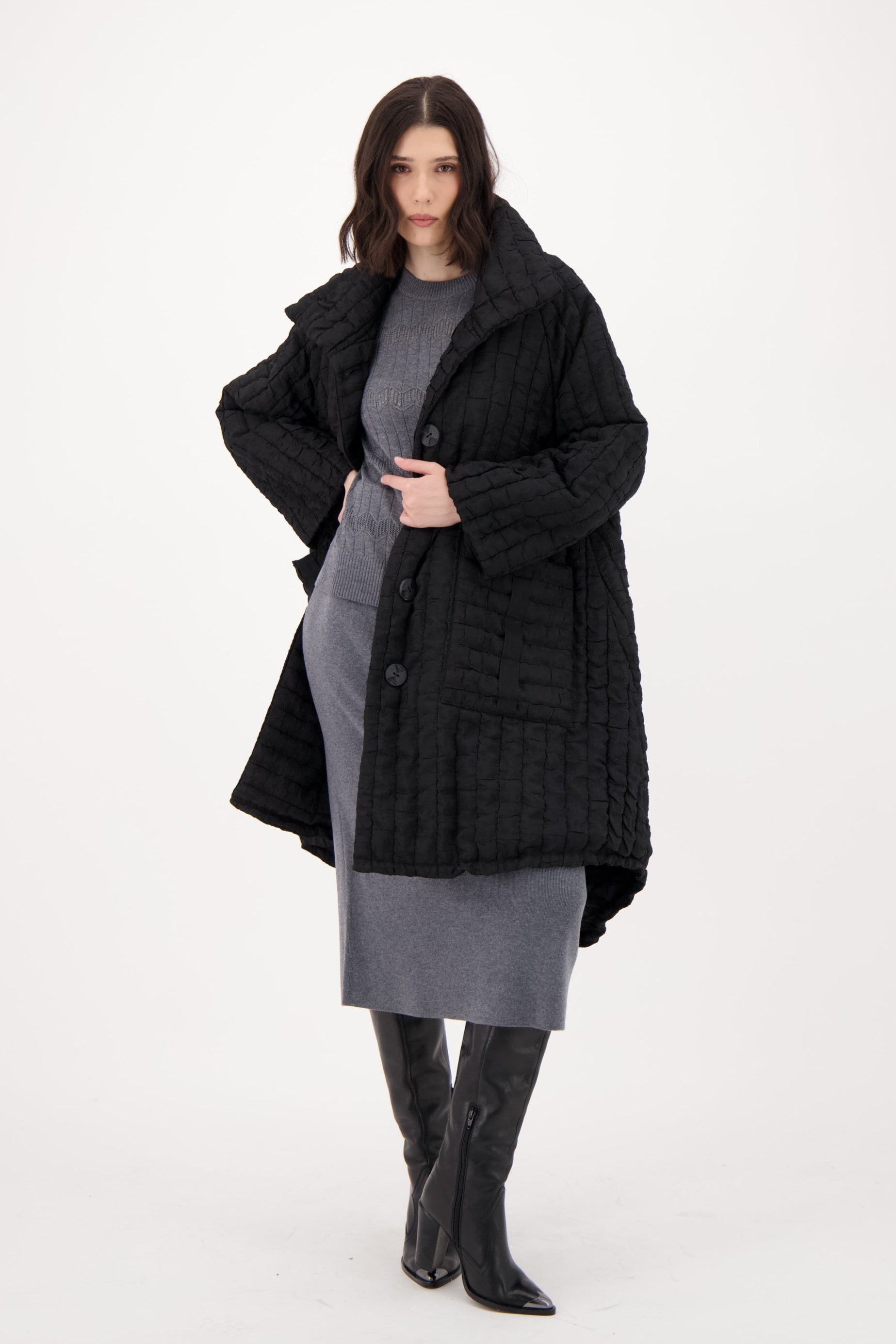 Woman wearing a black coat, gray dress, and black boots on a white background