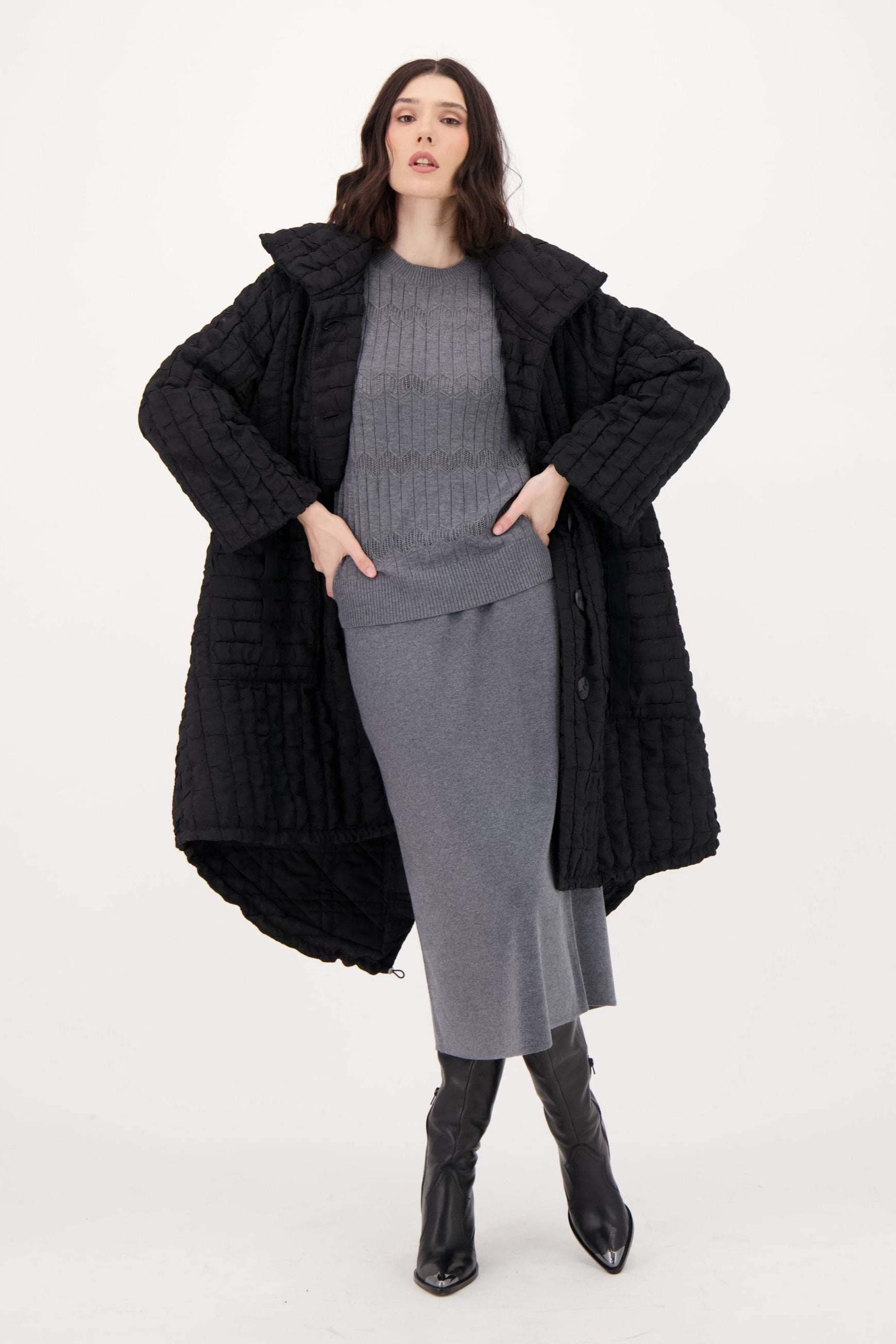 Woman wearing a long black coat over a gray outfit on a white background