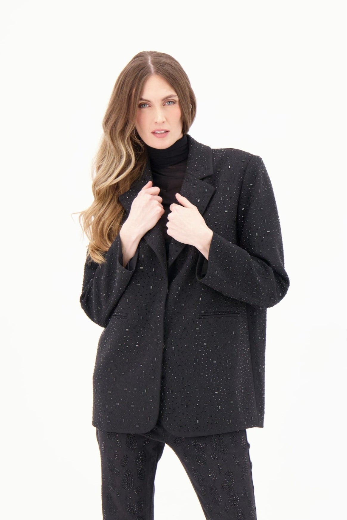Woman wearing a black textured blazer over a black turtleneck on a white background