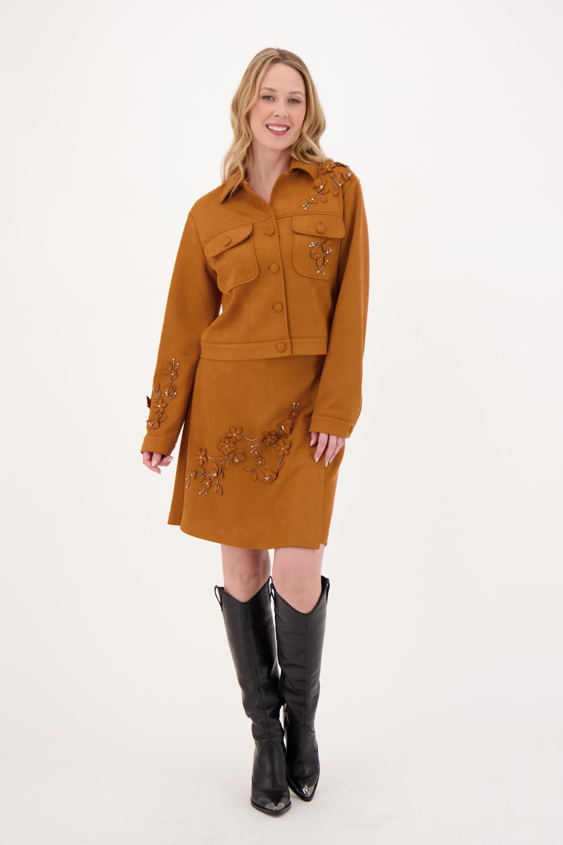 Woman wearing a mustard yellow dress with embroidery and black knee-high boots on a white background 