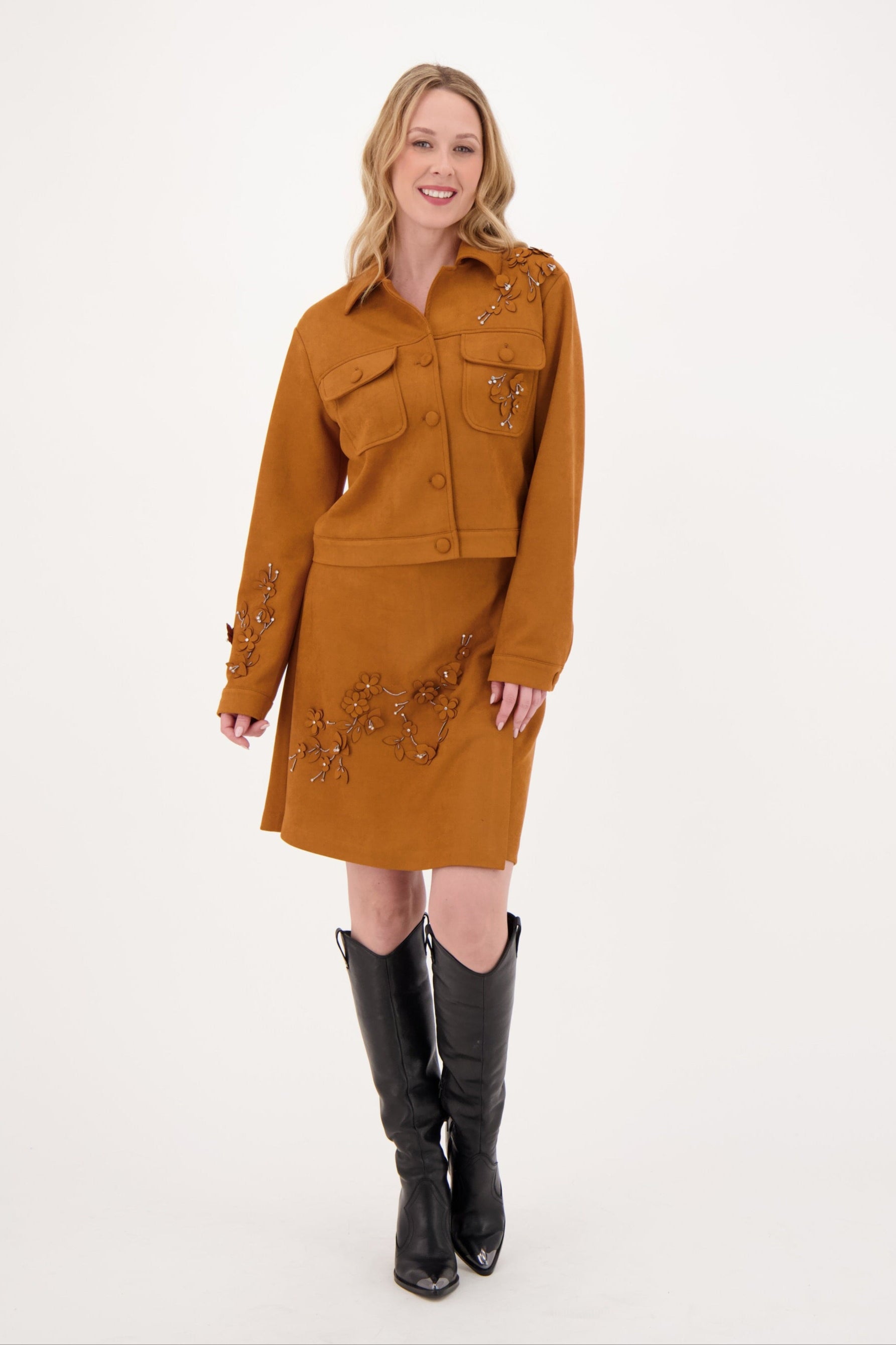 Woman wearing a mustard yellow dress with embroidery and black knee-high boots on a white background