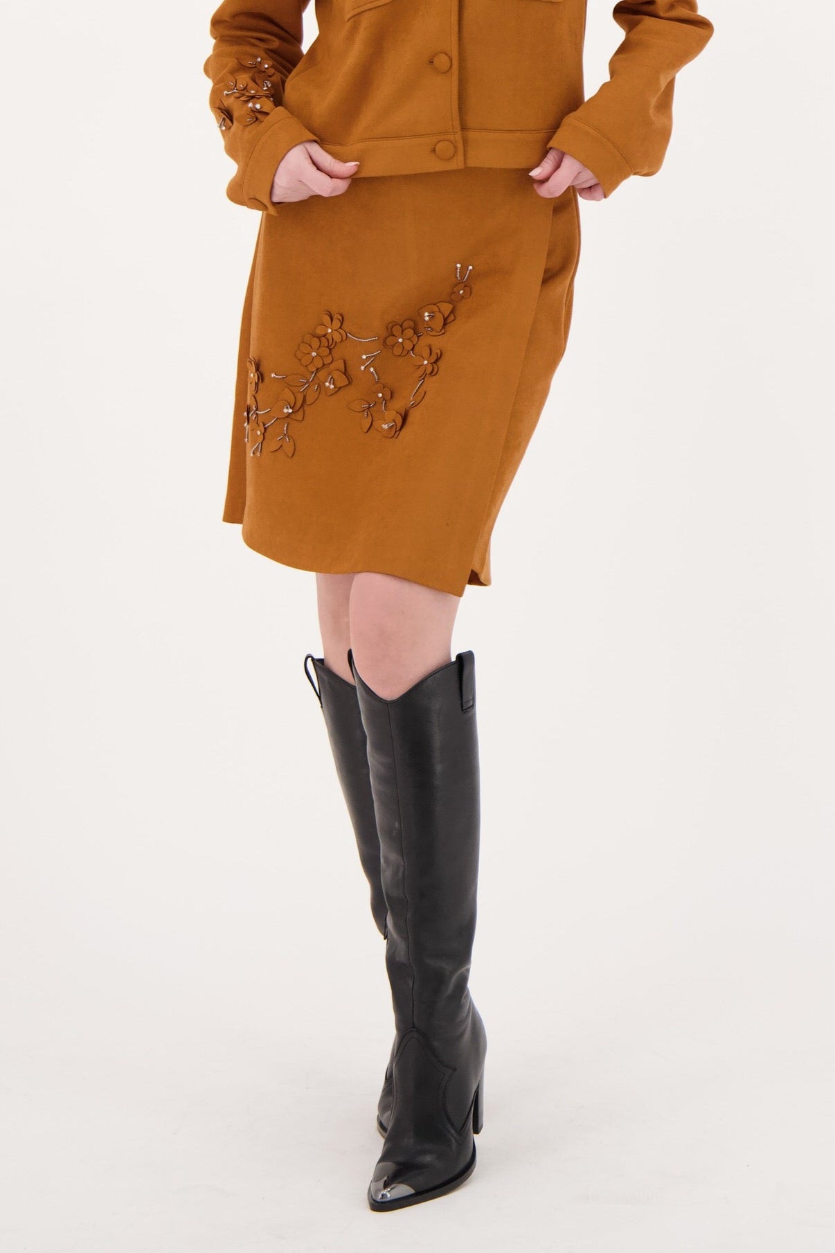 Woman wearing a mustard yellow dress with black knee-high boots on a white background