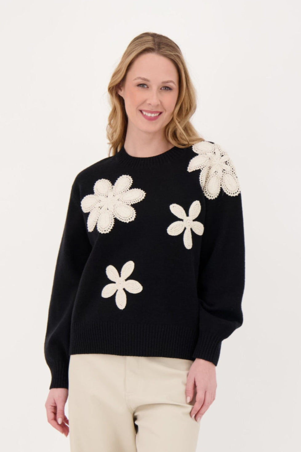 Woman wearing a black sweater with white floral patterns on a plain background