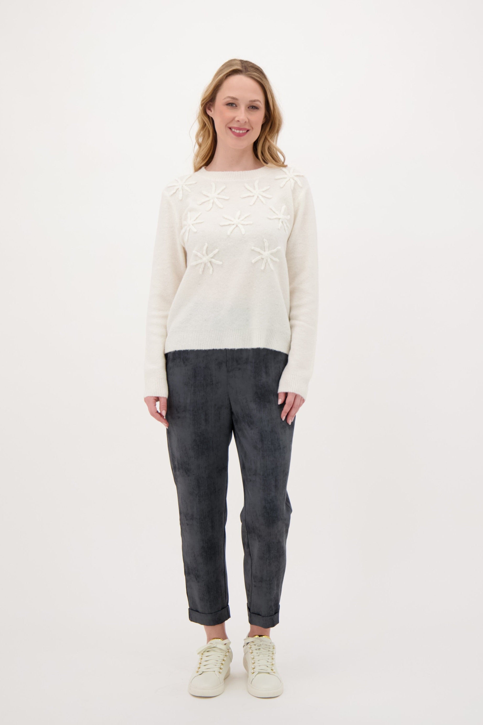Woman wearing a white sweater and dark pants on a white background