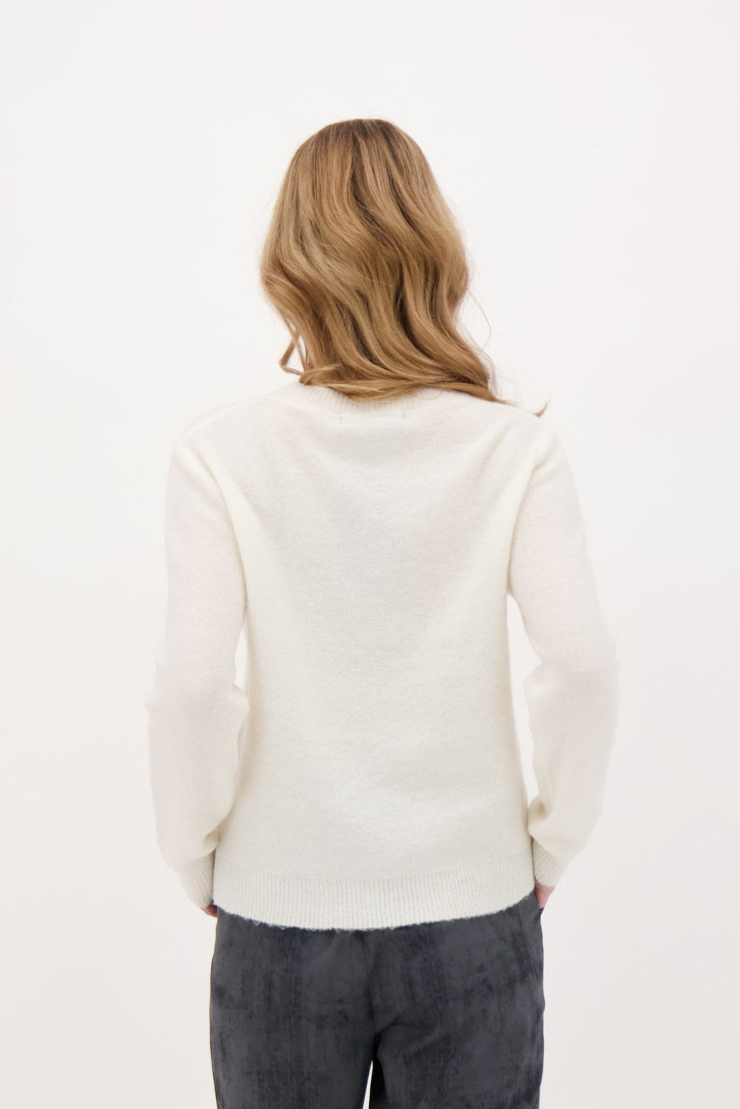 Person wearing a white sweater and dark pants on a plain background