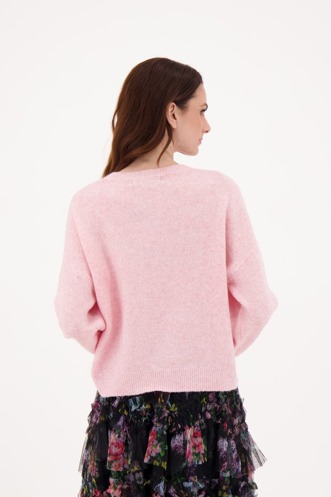 Woman wearing a pink sweater and floral skirt on a white background