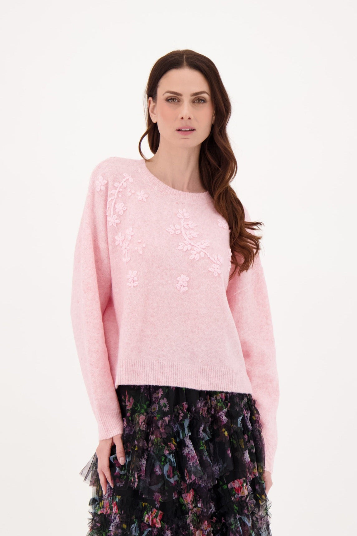 Woman wearing a light pink sweater with a floral skirt on a white background