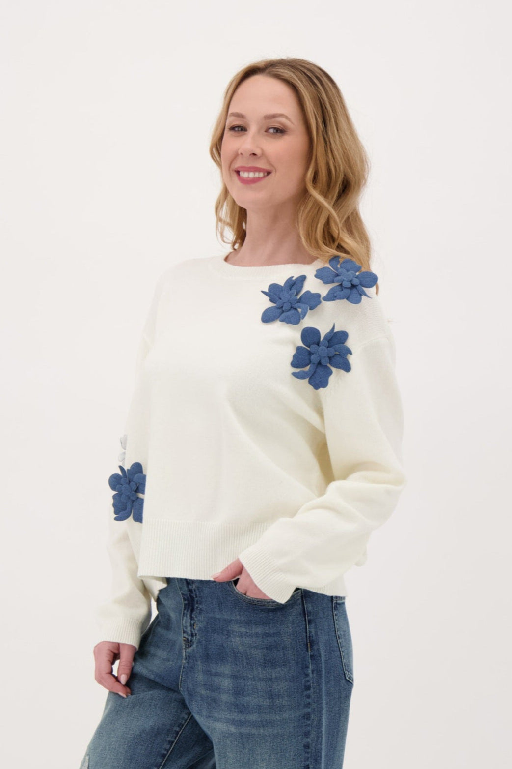 Woman wearing a white sweater with blue floral patterns on a plain background