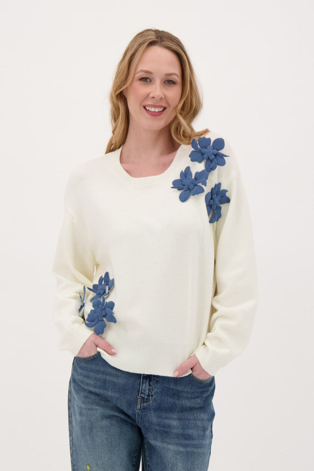 Woman wearing a cream sweater with blue floral patterns on a white background