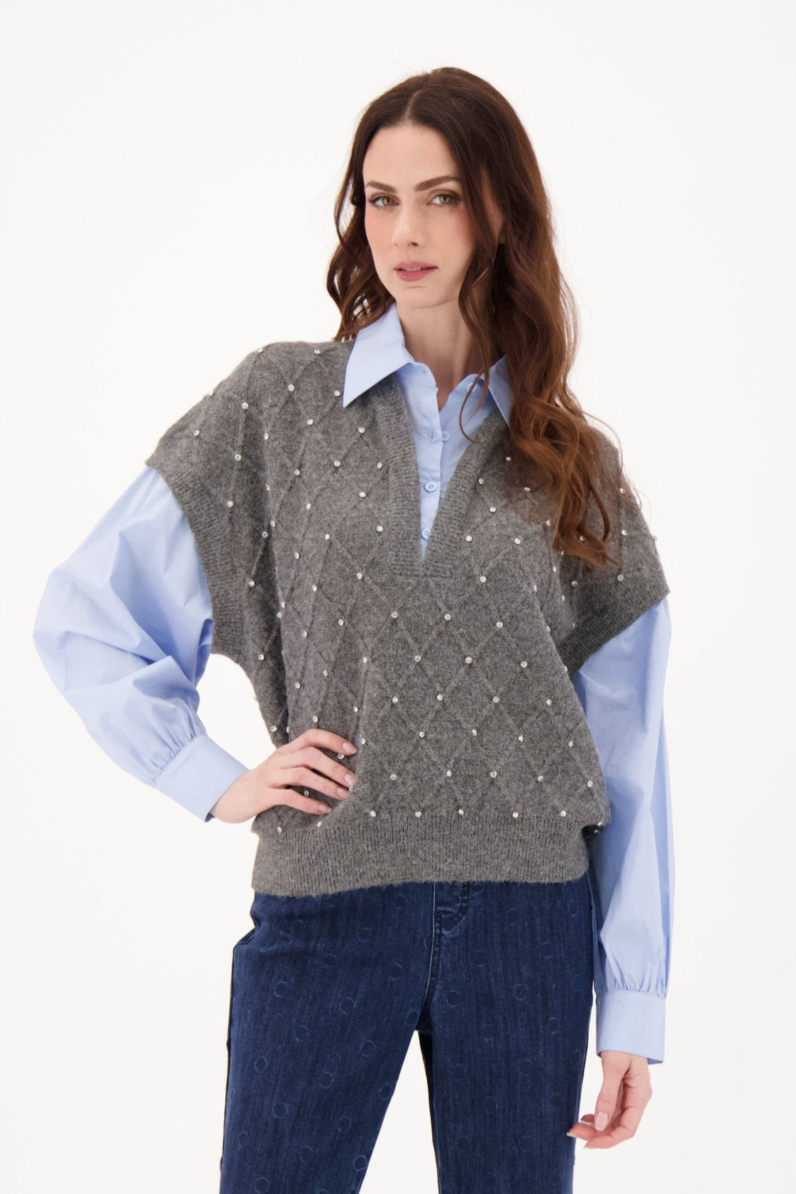 Woman wearing a gray patterned sweater over a light blue shirt with dark blue jeans on a white background