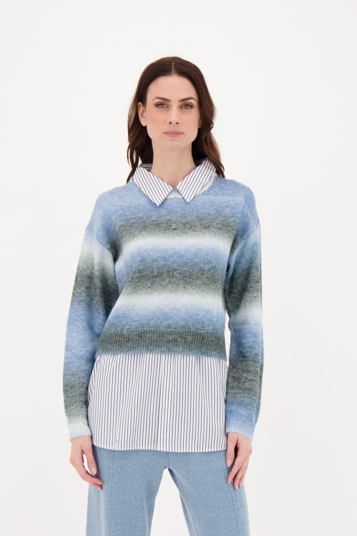 Woman wearing a blue and gray striped sweater over a white collared shirt on a white background
