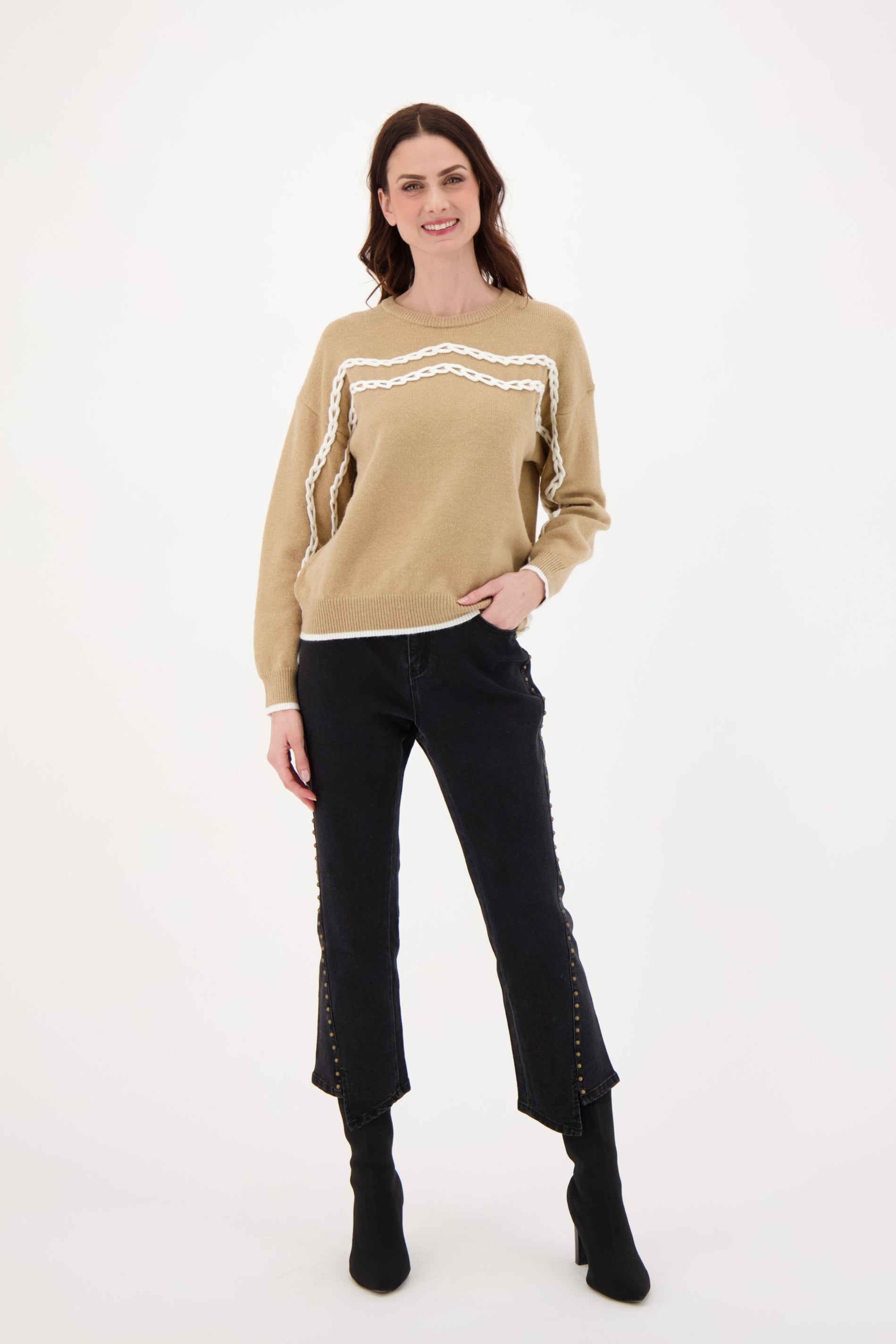 Woman wearing a beige sweater with white lace details and black jeans on a white background