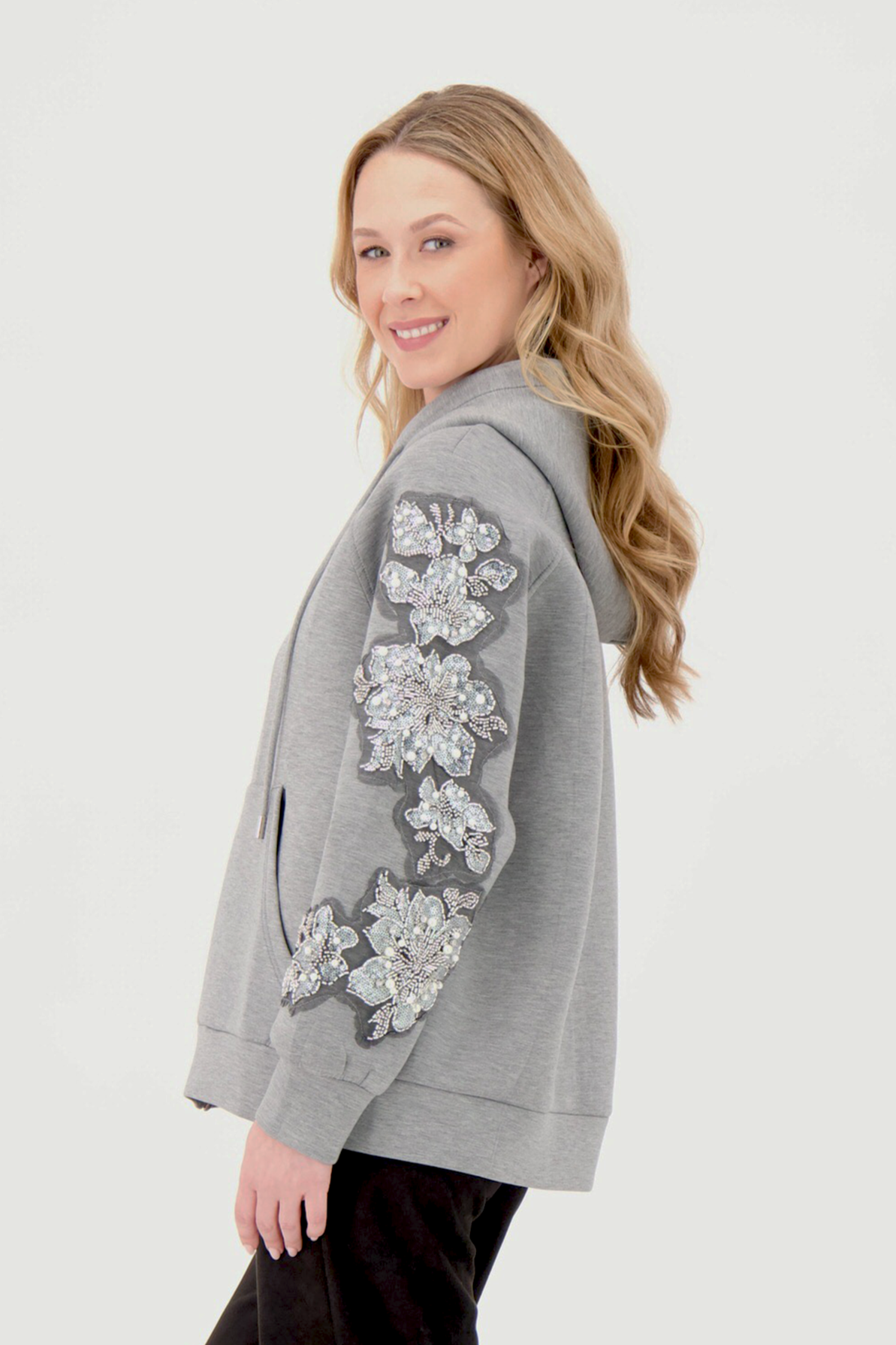 Woman wearing a gray cardigan with floral embroidery on a white background