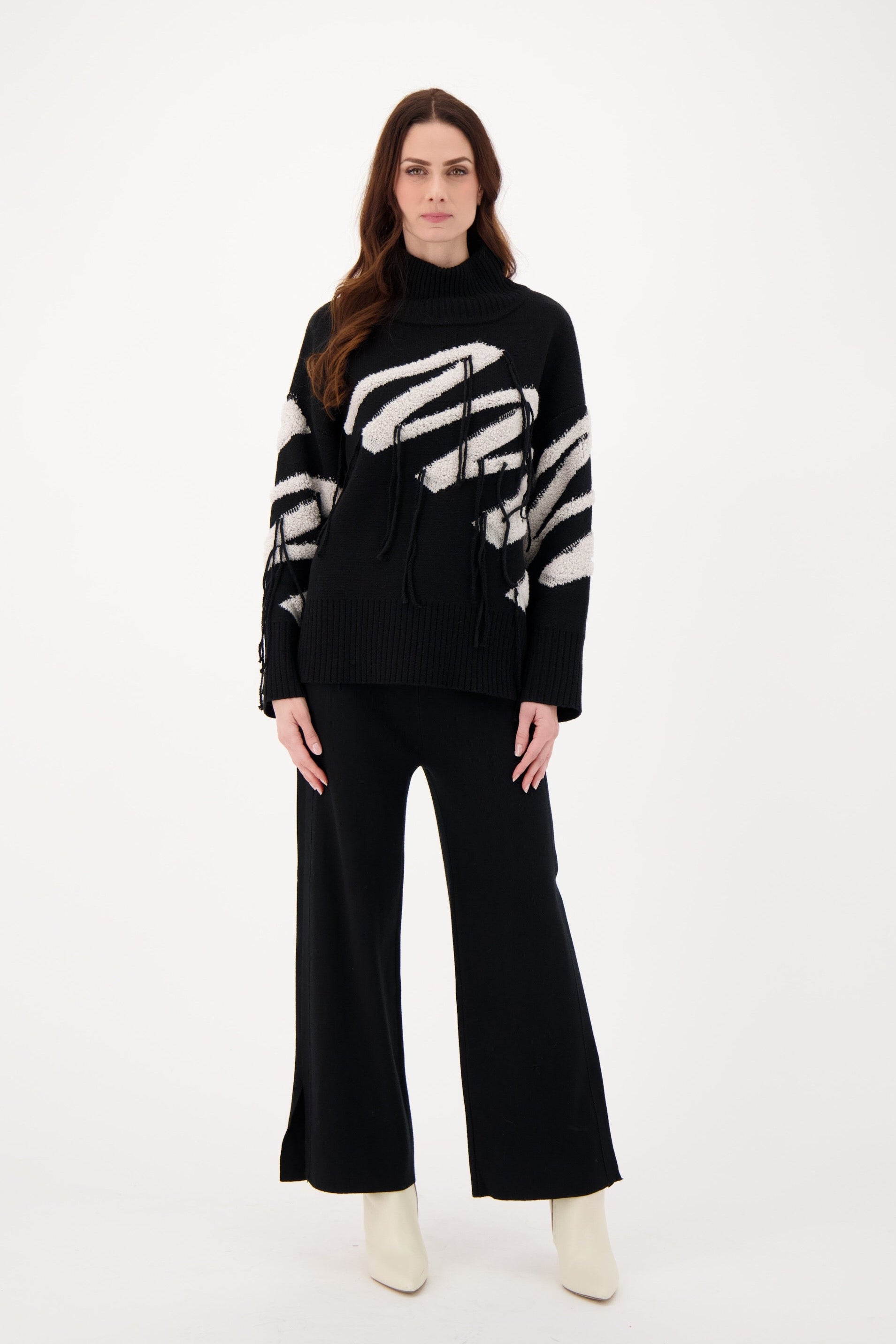 Woman wearing a black sweater with white hand design and black pants on a white background