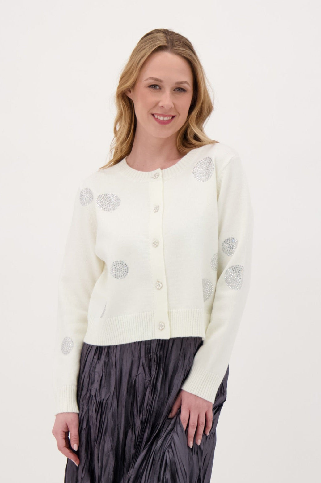 Woman wearing a white sweater with gray buttons and a dark pleated skirt on a white background