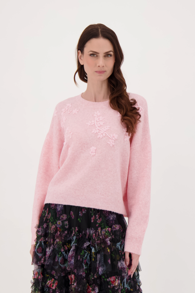 Woman wearing a pink sweater and floral skirt on a white background