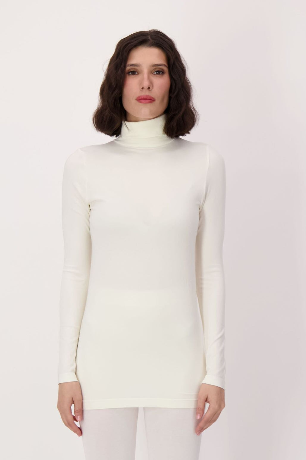 Woman wearing a white turtleneck and leggings against a plain background