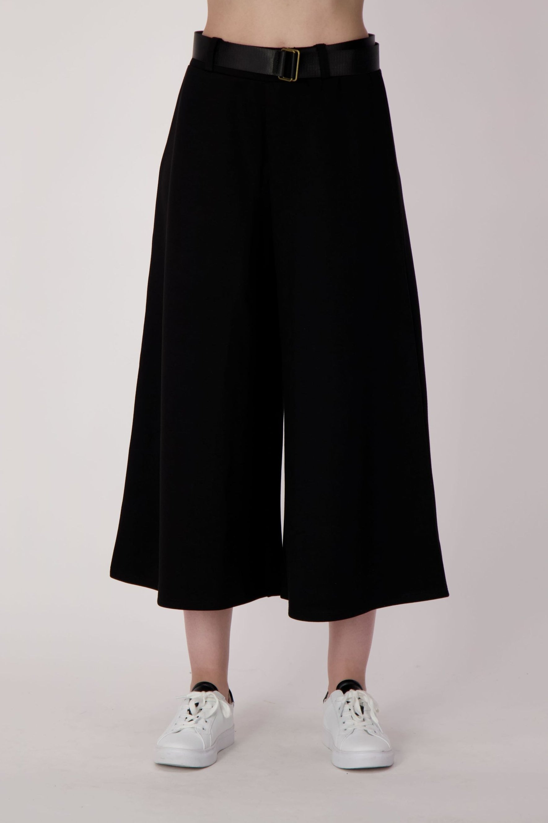 Person wearing black wide-leg pants and white sneakers on a plain background